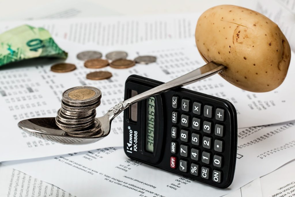 A spoon balancing on a calculator with coins on one end and a potato on the other.