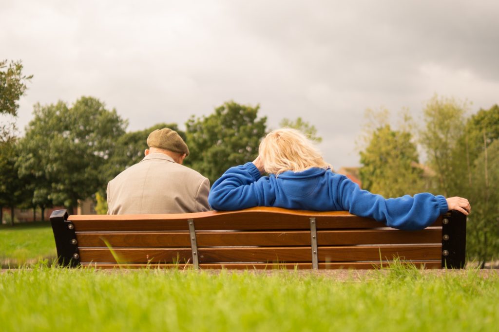 An old couple sitting on a bench facing away from the camera.