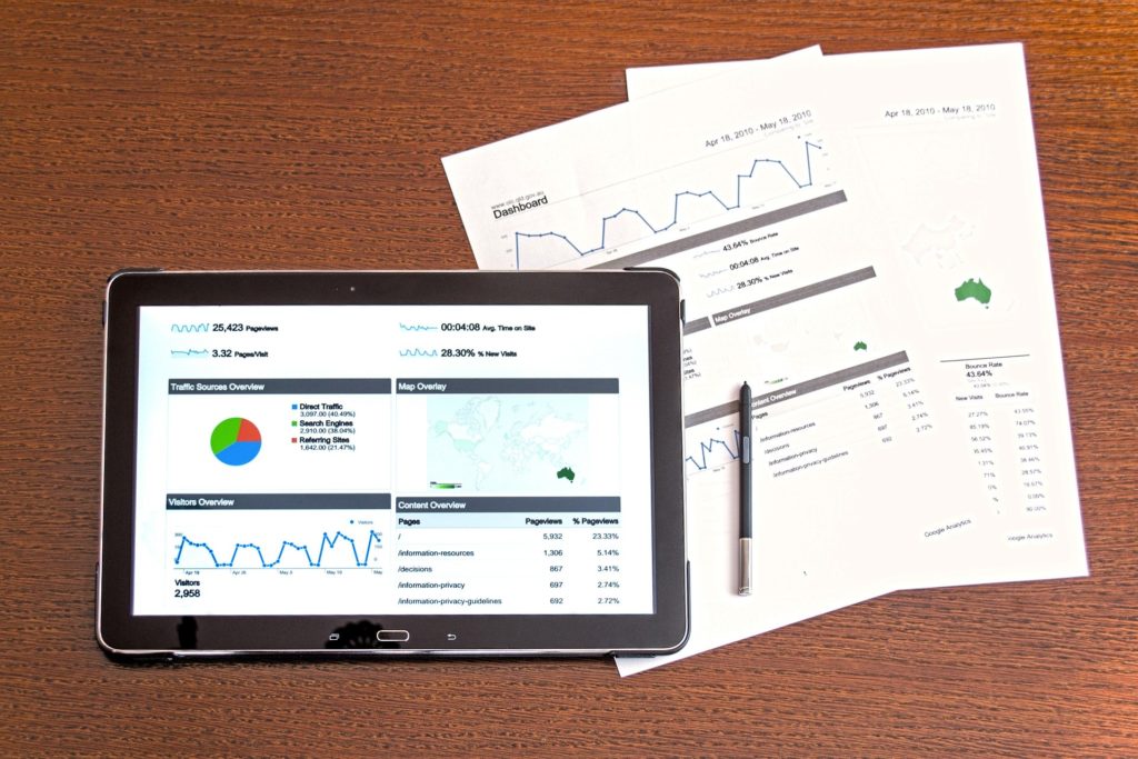 A tablet computer displaying financial graphs lays on a wooden table beside two physical financial statements and a pen.