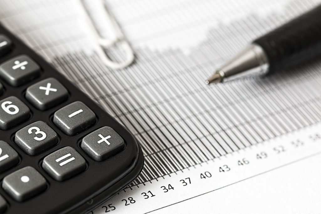 A calculator resting on top of a spreadsheet beside a pen.