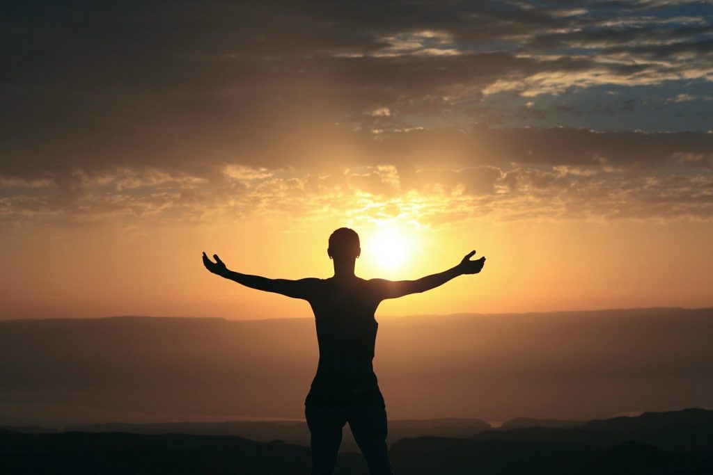 A silhouette of a woman facing the sunset with her arms outstretched.