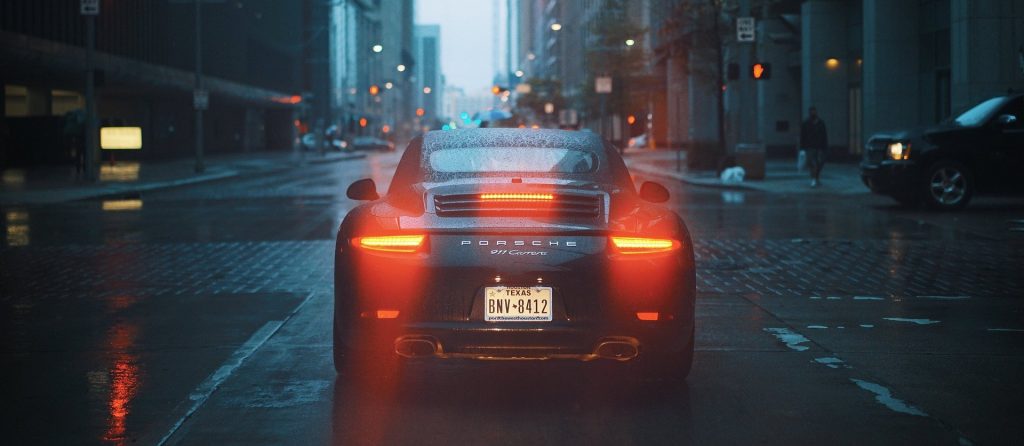 The rear end of a Porsche on a rainy city street.