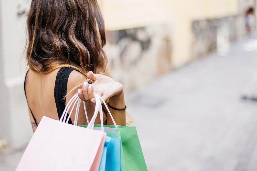 A woman with brown hair holding shopping bags behind her.